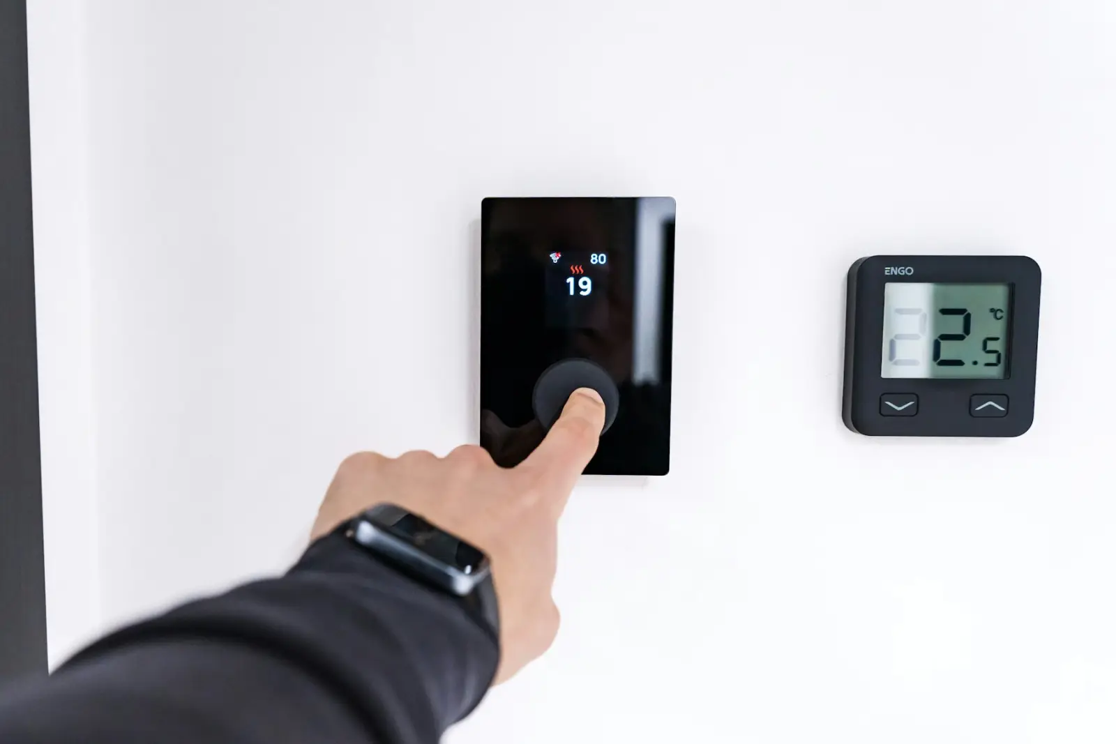 A finger adjusting a wall-mounted thermostat